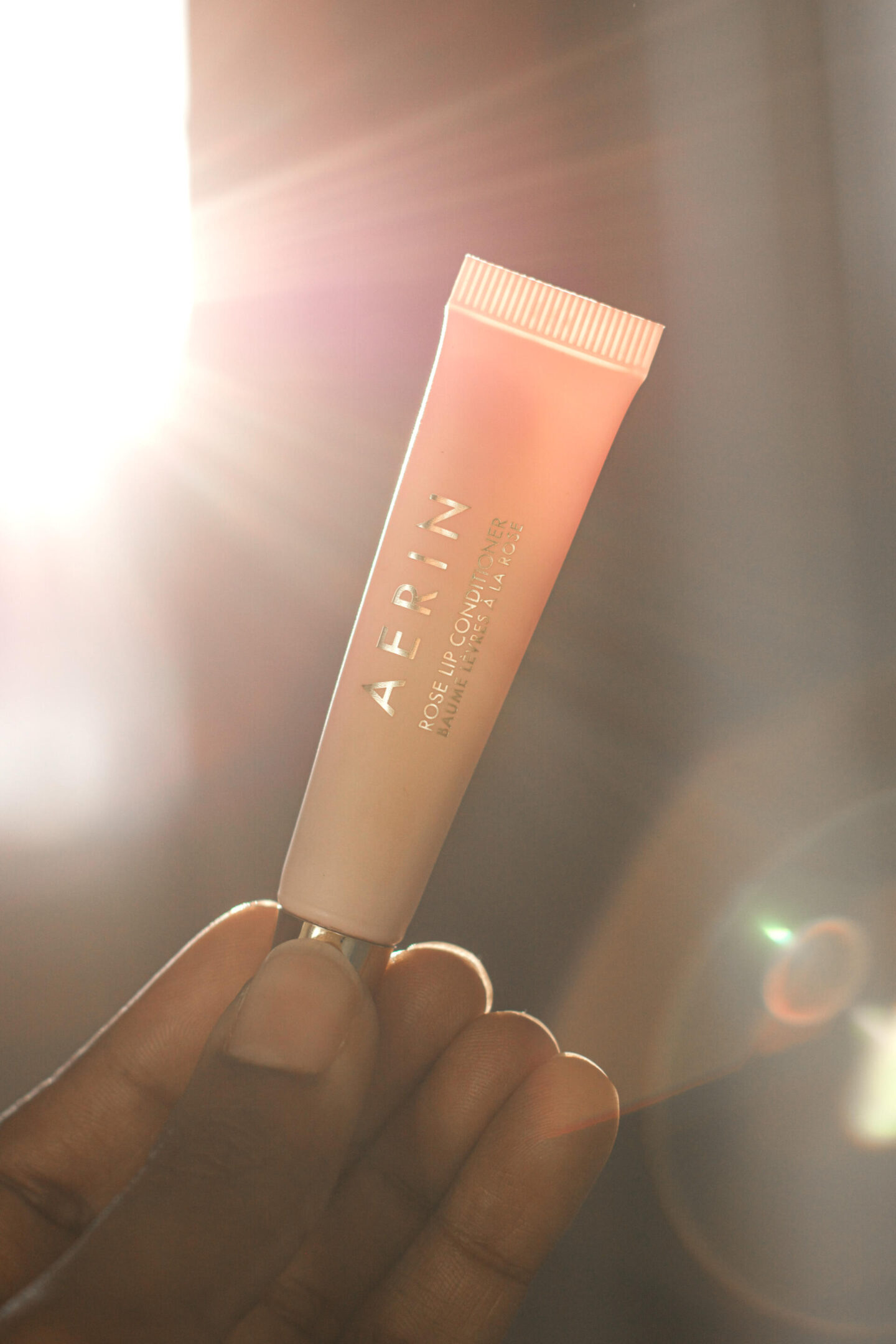 Aerin Rose Lip Conditioner held in front of the sun